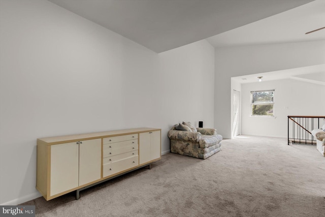 sitting room with vaulted ceiling, light colored carpet, an upstairs landing, and ceiling fan