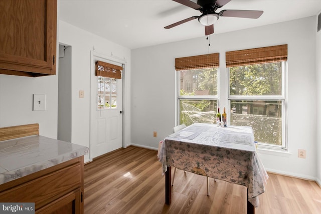 dining area with light wood finished floors, a ceiling fan, and baseboards