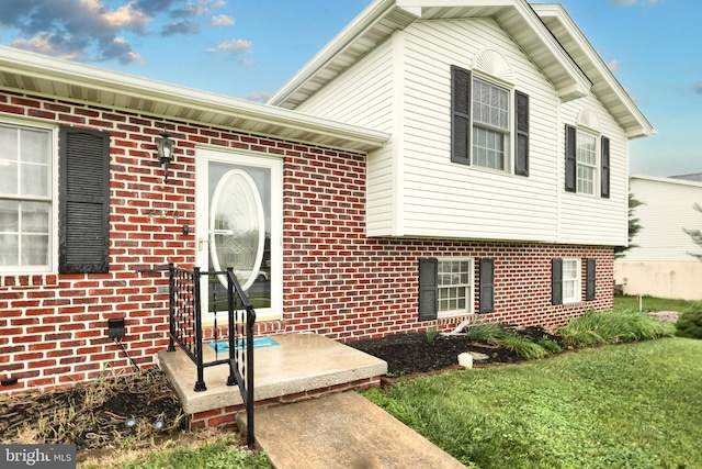 view of exterior entry featuring brick siding and a yard