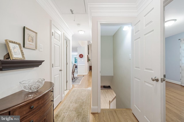 hallway featuring attic access, light wood finished floors, baseboards, and crown molding