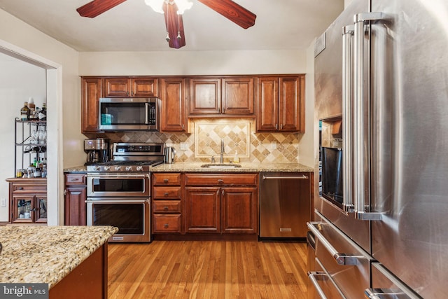 kitchen with stainless steel appliances, a sink, ceiling fan, light wood-style flooring, and tasteful backsplash