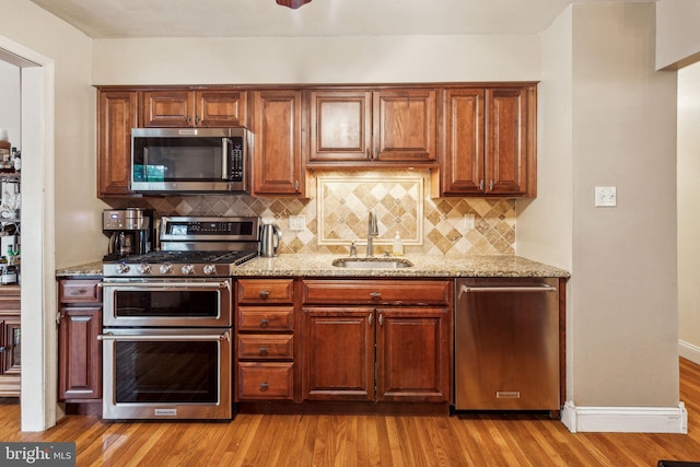 kitchen with appliances with stainless steel finishes, a sink, decorative backsplash, and light stone countertops