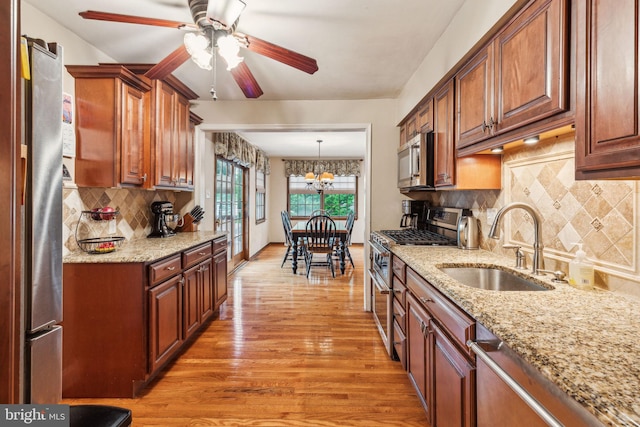 kitchen with appliances with stainless steel finishes, a sink, ceiling fan, light wood-style flooring, and decorative backsplash