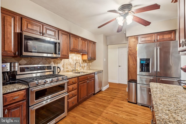 kitchen with appliances with stainless steel finishes, a sink, a ceiling fan, backsplash, and light wood-style flooring