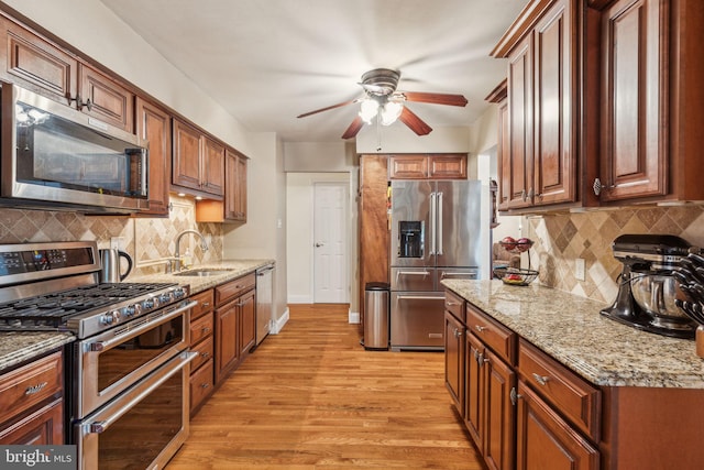 kitchen with stainless steel appliances, a sink, ceiling fan, light wood-type flooring, and tasteful backsplash