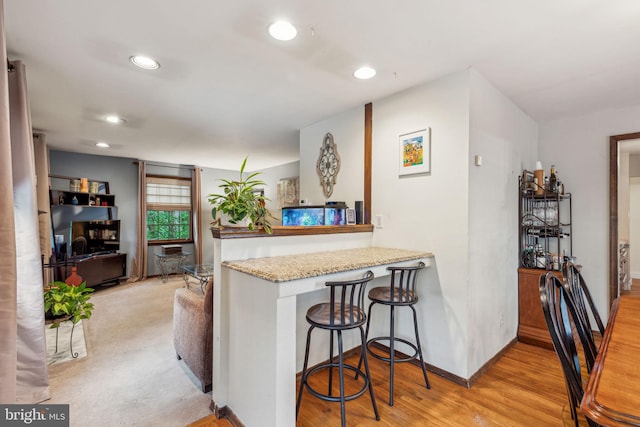 kitchen featuring recessed lighting, a breakfast bar area, baseboards, a peninsula, and light stone countertops