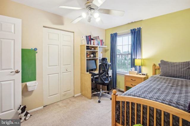 bedroom featuring light colored carpet, a closet, a desk, baseboards, and ceiling fan
