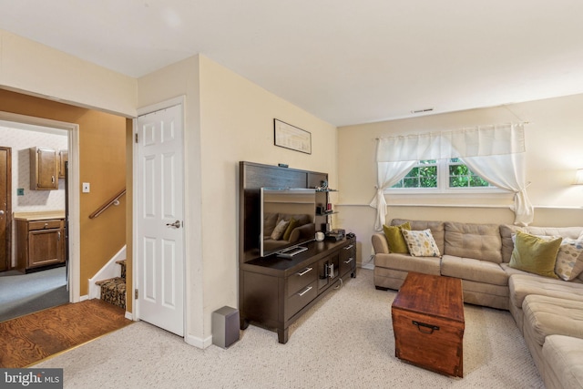 living area with light carpet, baseboards, and stairway