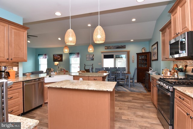 kitchen with stainless steel appliances, a sink, a kitchen island, tasteful backsplash, and light stone counters