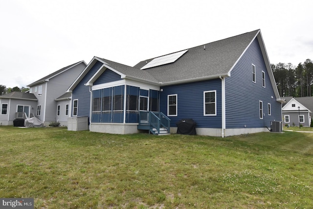 back of property with central AC, a sunroom, roof mounted solar panels, and a lawn