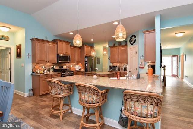 kitchen featuring stainless steel appliances, a kitchen breakfast bar, lofted ceiling, backsplash, and wood finished floors