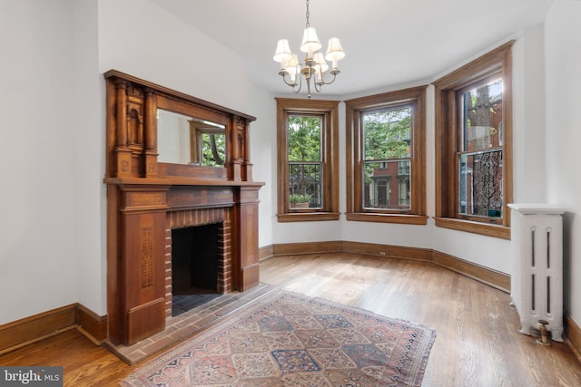 108 3rd St NE, Washington, DC 20002 - unfurnished living room with radiator heating unit, a chandelier, light wood-style floors, and a brick fireplace