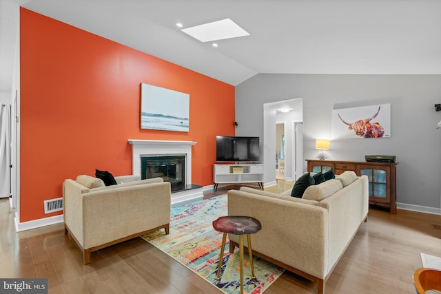 living area featuring vaulted ceiling, wood finished floors, a glass covered fireplace, baseboards, and a skylight