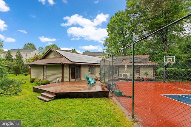 rear view of property featuring roof mounted solar panels, a wooden deck, and basketball court