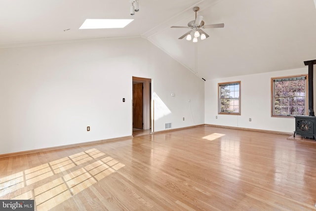 unfurnished living room featuring a wood stove, a ceiling fan, a skylight, light wood-style floors, and high vaulted ceiling