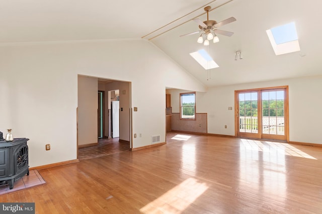 unfurnished living room with a skylight, a wood stove, high vaulted ceiling, ceiling fan, and baseboards