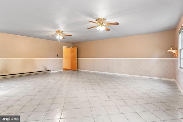spare room featuring wainscoting, ceiling fan, a baseboard heating unit, baseboards, and wallpapered walls