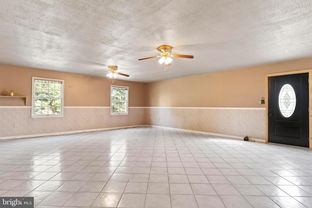 unfurnished room with a wainscoted wall, a textured ceiling, ceiling fan, and tile patterned floors