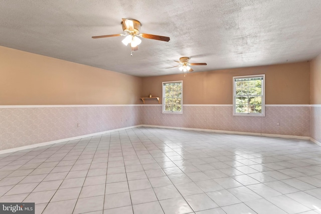 unfurnished room featuring a wainscoted wall, a textured ceiling, healthy amount of natural light, ceiling fan, and baseboards