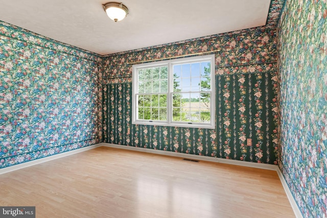 spare room with wood finished floors, wallpapered walls, and baseboards
