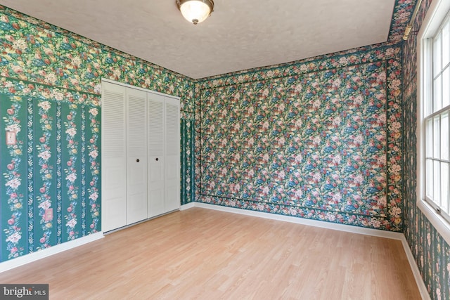 unfurnished bedroom featuring wallpapered walls, wood finished floors, baseboards, a closet, and a textured ceiling