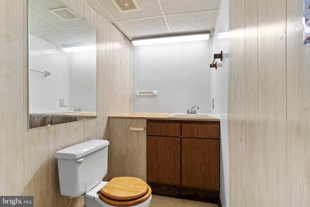 half bathroom featuring toilet, wood walls, and vanity