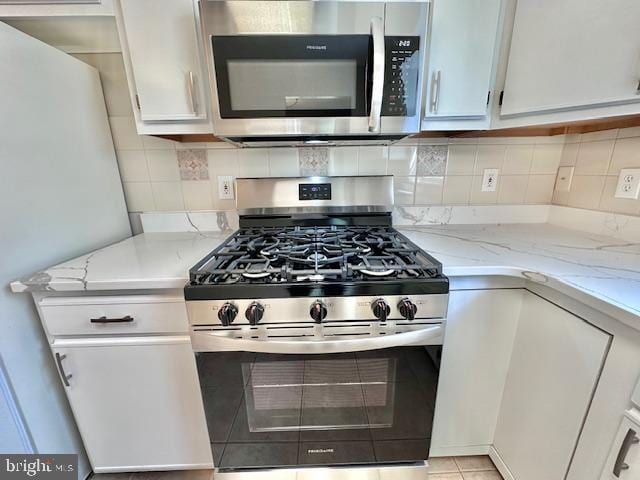kitchen featuring appliances with stainless steel finishes, white cabinets, light stone counters, and decorative backsplash
