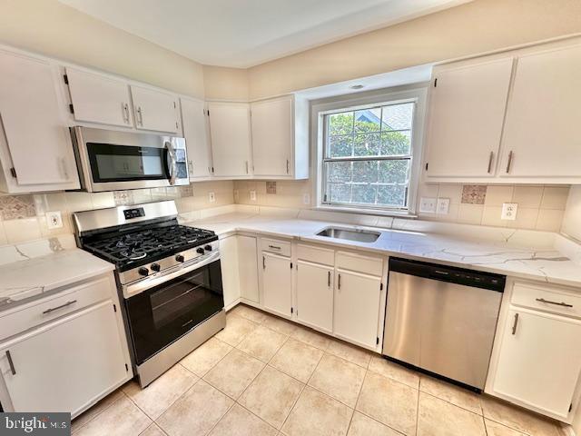 kitchen featuring appliances with stainless steel finishes, light tile patterned flooring, backsplash, and white cabinetry