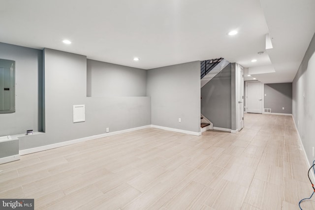finished basement with stairway, electric panel, baseboards, recessed lighting, and light wood finished floors