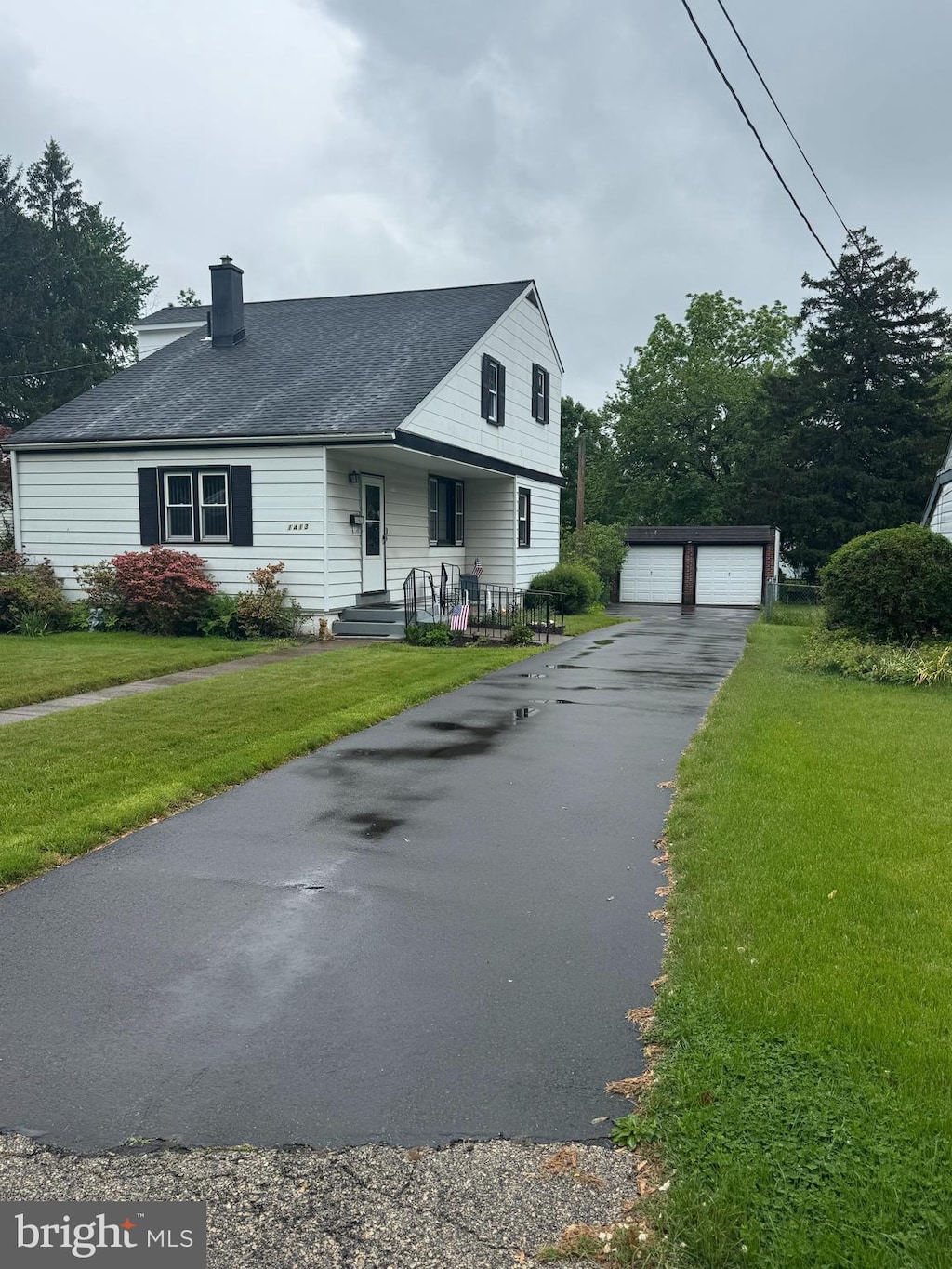 view of front of house featuring an outdoor structure, a chimney, a detached garage, and a front lawn