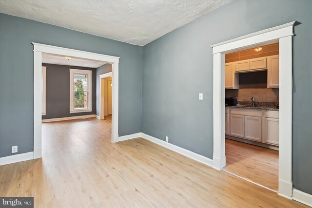 1081 Ellicott Dr, Baltimore, MD 21216 - unfurnished room featuring light wood-type flooring, a sink, baseboards, and a textured ceiling
