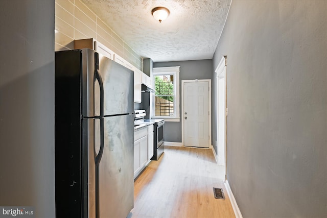 1081 Ellicott Dr, Baltimore, MD 21216 - kitchen with stainless steel appliances, white cabinets, light wood-type flooring, a textured ceiling, and baseboards