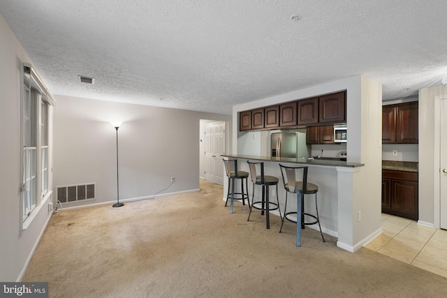 13113 Briarcliff Ter Unit 1-101, Germantown, MD 20874 - kitchen featuring appliances with stainless steel finishes, a kitchen bar, light colored carpet, a textured ceiling, and dark brown cabinets