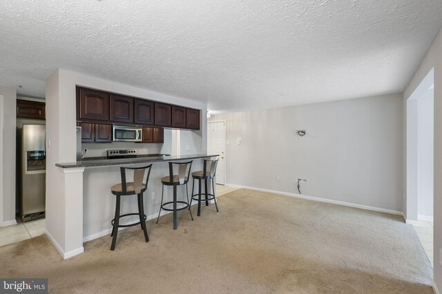 13113 Briarcliff Ter Unit 1-101, Germantown, MD 20874 - kitchen featuring stainless steel appliances, light colored carpet, dark countertops, a breakfast bar area, and dark brown cabinets