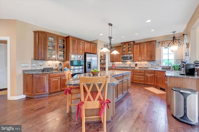 kitchen with appliances with stainless steel finishes, brown cabinets, wood finished floors, light stone counters, and recessed lighting