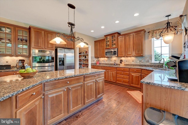 kitchen featuring stainless steel appliances, a sink, light wood-style flooring, brown cabinetry, and recessed lighting
