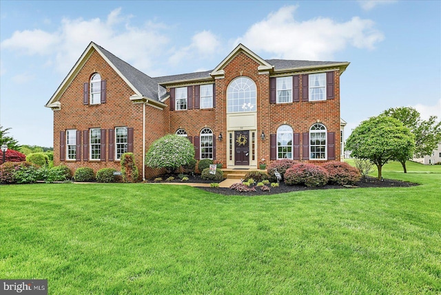 colonial house featuring a front yard, brick siding, and roof with shingles