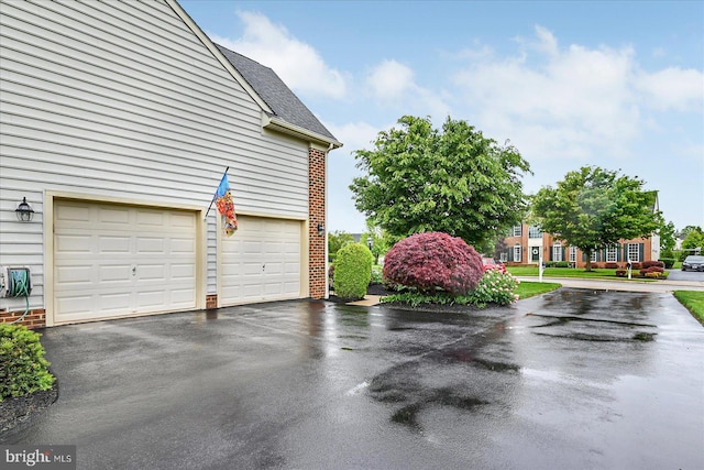 view of property exterior with asphalt driveway, a garage, a shingled roof, and brick siding