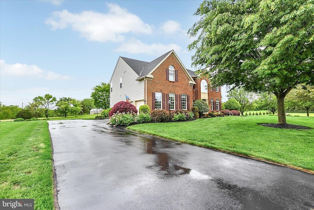 view of side of property featuring brick siding, asphalt driveway, an attached garage, and a yard