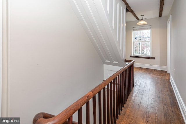 corridor with dark wood-type flooring, baseboards, beamed ceiling, and an upstairs landing