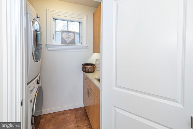 washroom with stacked washing machine and dryer, baseboards, and light tile patterned floors