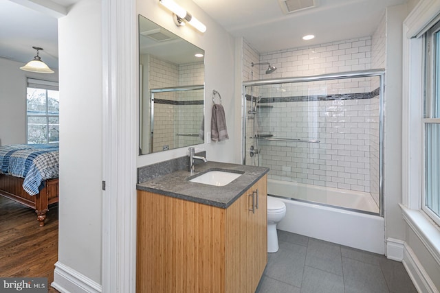 ensuite bathroom featuring combined bath / shower with glass door, vanity, toilet, tile patterned floors, and baseboards