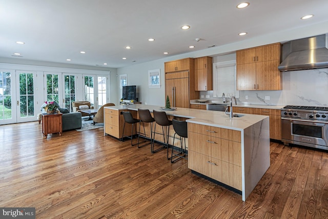 kitchen with premium appliances, wall chimney exhaust hood, wood finished floors, recessed lighting, and a sink