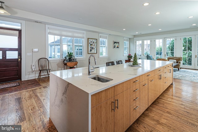 kitchen with a sink, light wood-type flooring, light stone counters, open floor plan, and recessed lighting