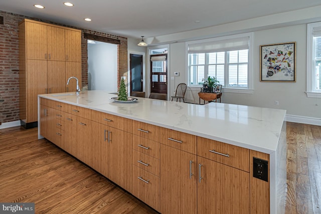 kitchen with wood finished floors, a sink, plenty of natural light, light stone counters, and recessed lighting