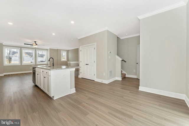 kitchen with a sink, crown molding, open floor plan, baseboards, and white cabinetry