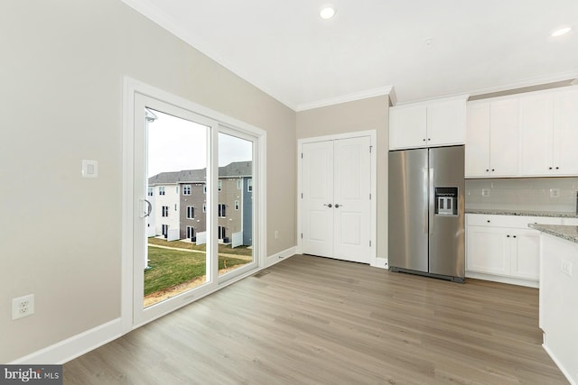 kitchen with stainless steel fridge, ornamental molding, light wood finished floors, white cabinets, and backsplash