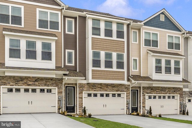 townhome / multi-family property with an attached garage, stone siding, and concrete driveway