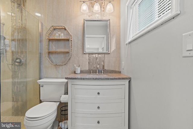 bathroom featuring a stall shower, vanity, toilet, and tile walls