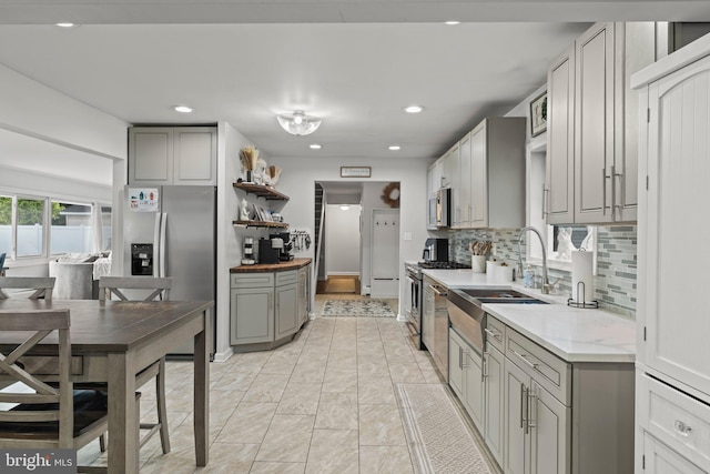 kitchen featuring gray cabinets, a sink, stainless steel appliances, open shelves, and backsplash